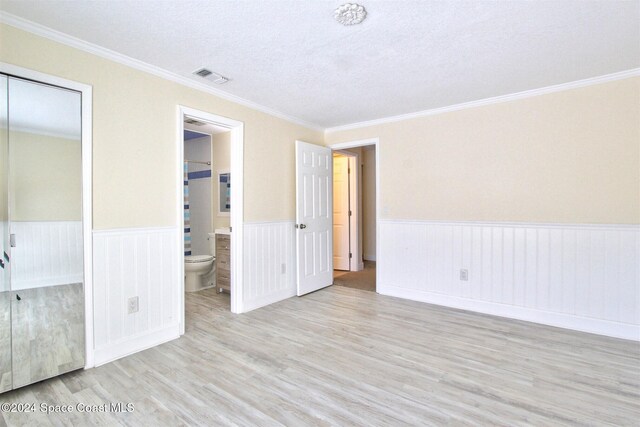 unfurnished bedroom featuring ensuite bathroom, light hardwood / wood-style flooring, a textured ceiling, and ornamental molding