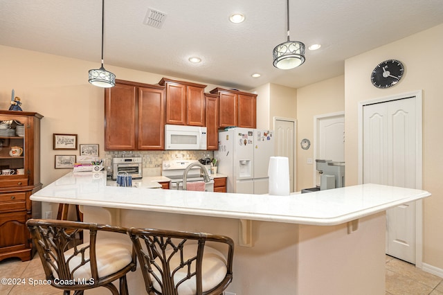 kitchen with a kitchen breakfast bar, light tile patterned flooring, pendant lighting, and white appliances