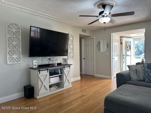 living room with ceiling fan, light wood-type flooring, and a textured ceiling