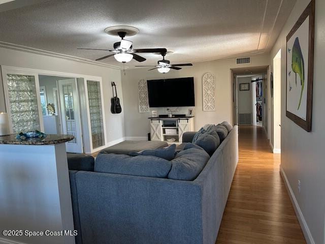 living room with hardwood / wood-style floors, a textured ceiling, ceiling fan, and crown molding