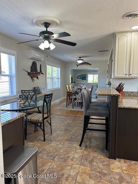 dining room featuring a wall mounted AC, ceiling fan, a healthy amount of sunlight, and a textured ceiling