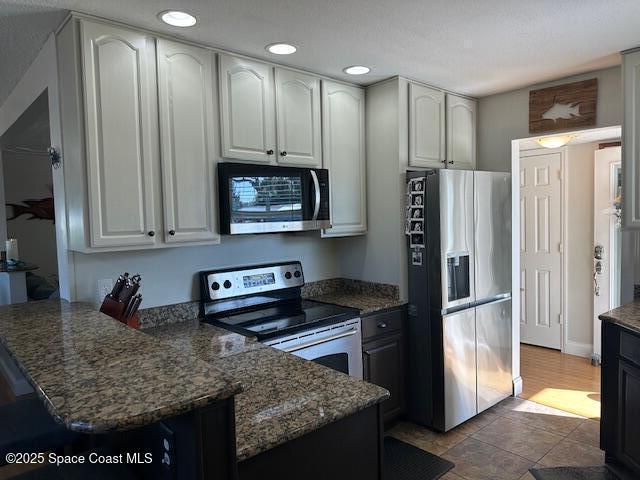 kitchen with white cabinets, appliances with stainless steel finishes, light tile patterned floors, and dark stone countertops