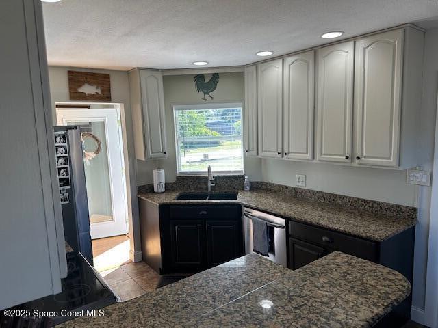 kitchen featuring black refrigerator, sink, light tile patterned floors, dishwasher, and white cabinetry