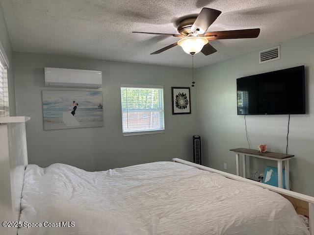 bedroom featuring a textured ceiling, an AC wall unit, and ceiling fan