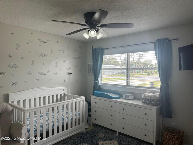 bedroom with a crib, a textured ceiling, and ceiling fan