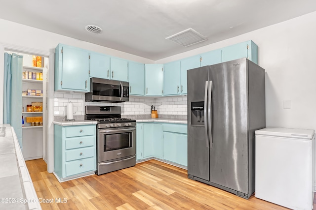 kitchen with decorative backsplash, stainless steel appliances, blue cabinets, and light hardwood / wood-style floors