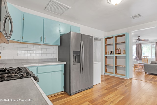 kitchen featuring blue cabinetry, ceiling fan, stainless steel appliances, backsplash, and light hardwood / wood-style floors