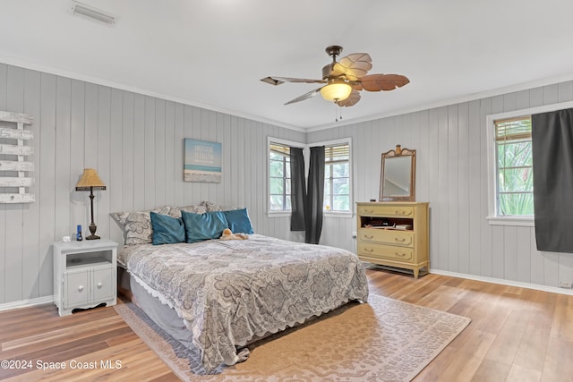 bedroom with multiple windows, ceiling fan, hardwood / wood-style floors, and wooden walls