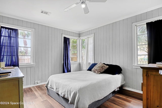 bedroom with crown molding, ceiling fan, wooden walls, and wood-type flooring