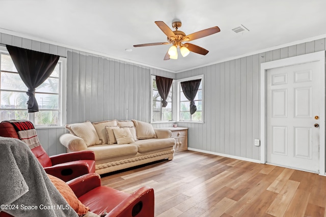 living room with hardwood / wood-style flooring, ceiling fan, wood walls, and ornamental molding