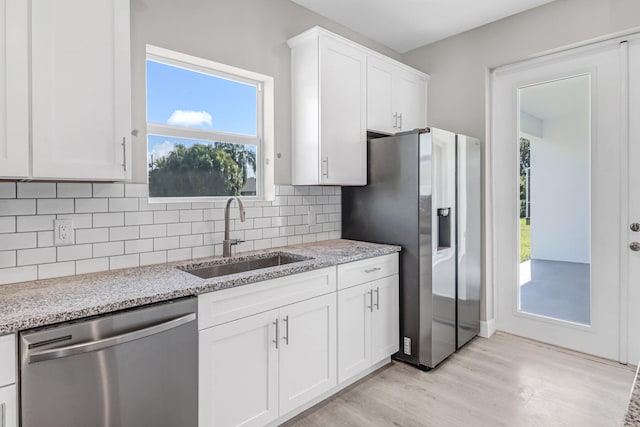 kitchen featuring light wood-type flooring, light stone counters, stainless steel appliances, sink, and white cabinets