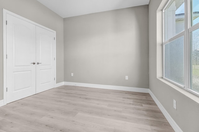 unfurnished bedroom featuring a closet, light wood-type flooring, and multiple windows