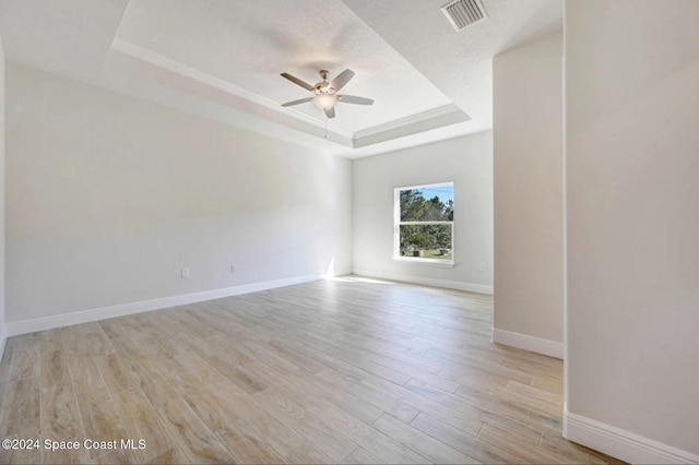 empty room featuring a raised ceiling, ceiling fan, and light wood-type flooring