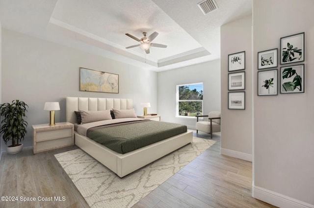 bedroom featuring ceiling fan, light wood-type flooring, and a tray ceiling