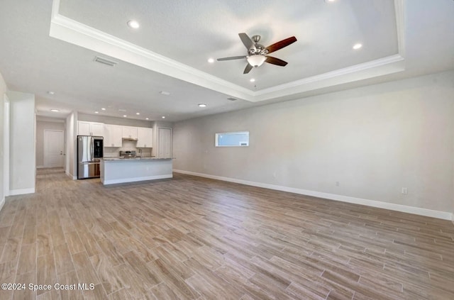 unfurnished living room featuring ceiling fan, ornamental molding, a tray ceiling, and light hardwood / wood-style flooring