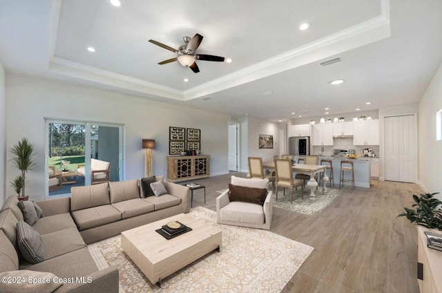 living room with ceiling fan, light hardwood / wood-style floors, a raised ceiling, and ornamental molding