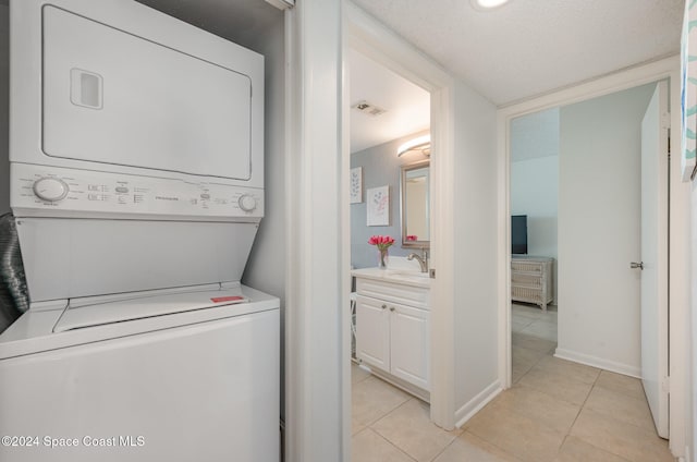 clothes washing area featuring a textured ceiling, sink, light tile patterned floors, and stacked washer and clothes dryer