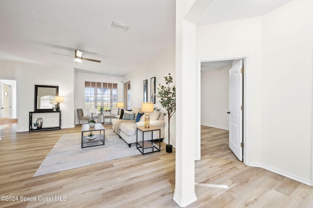 living room with a textured ceiling, light wood-type flooring, and ceiling fan