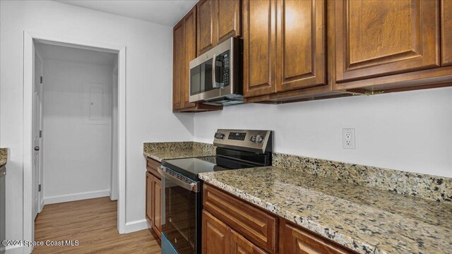 kitchen with light stone countertops, appliances with stainless steel finishes, and light hardwood / wood-style floors