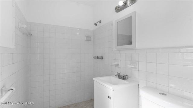 bathroom featuring tiled shower, vanity, toilet, and tile walls