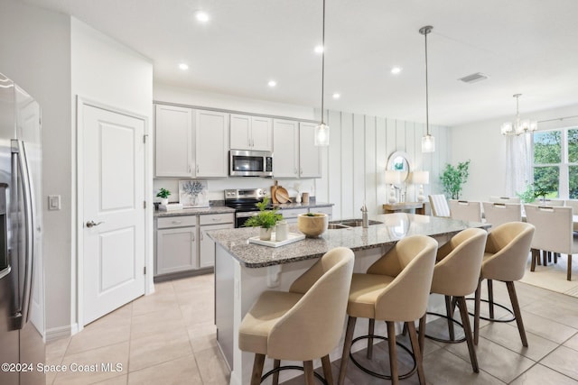 kitchen with hanging light fixtures, a kitchen breakfast bar, light stone counters, an island with sink, and appliances with stainless steel finishes