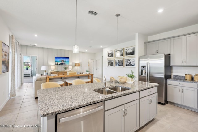 kitchen with sink, hanging light fixtures, light stone counters, a center island with sink, and appliances with stainless steel finishes