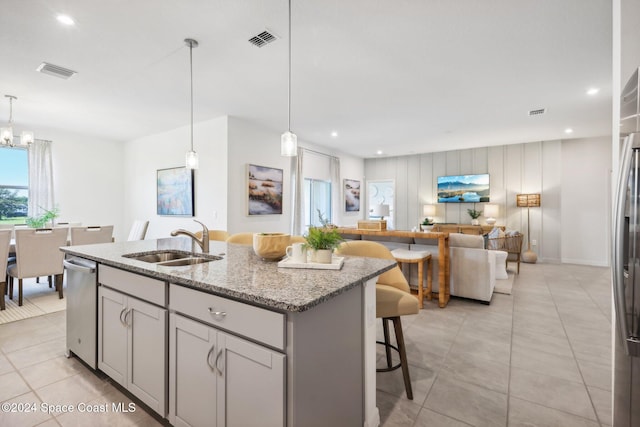 kitchen with light stone countertops, gray cabinetry, sink, hanging light fixtures, and an island with sink