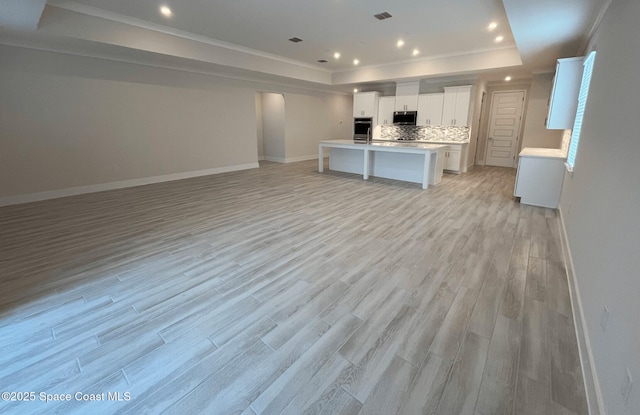 kitchen with light hardwood / wood-style flooring, stainless steel appliances, white cabinets, a center island with sink, and a raised ceiling