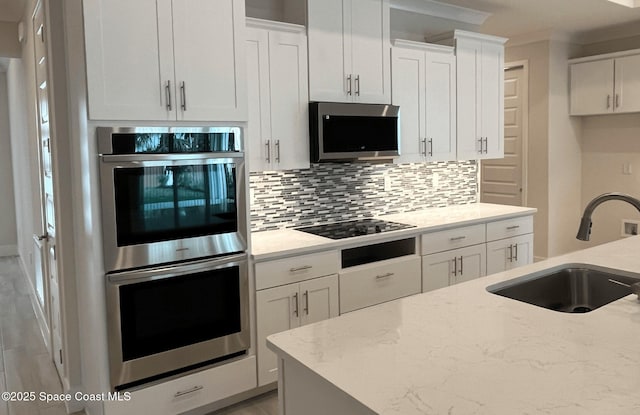 kitchen featuring decorative backsplash, appliances with stainless steel finishes, light stone countertops, sink, and white cabinetry