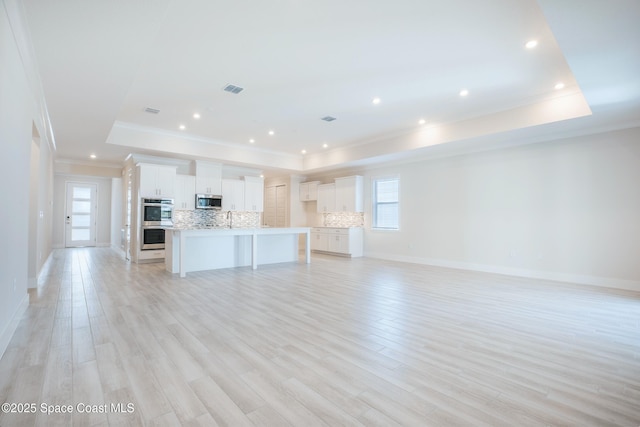 kitchen with appliances with stainless steel finishes, a kitchen island with sink, white cabinets, decorative backsplash, and a raised ceiling