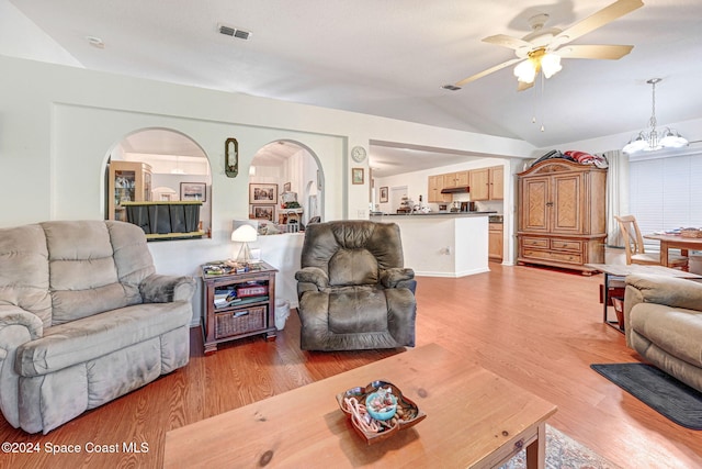 living room with ceiling fan with notable chandelier, hardwood / wood-style flooring, and vaulted ceiling