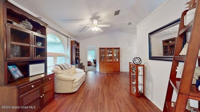 living area featuring visible vents, a ceiling fan, lofted ceiling, dark wood-style flooring, and a textured ceiling