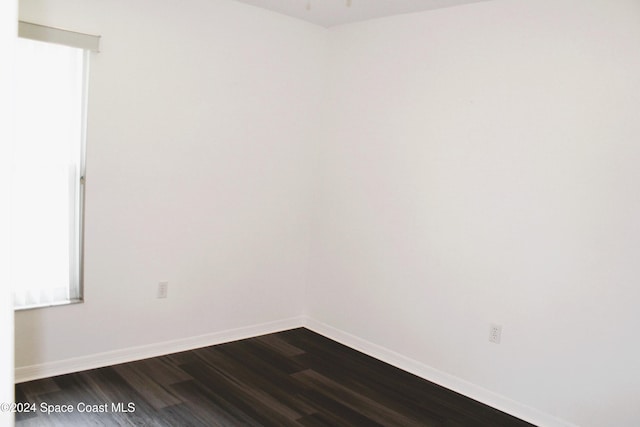 spare room with baseboards and dark wood-style flooring