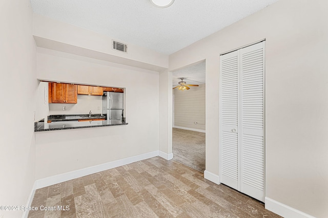 kitchen with a textured ceiling, light hardwood / wood-style flooring, stainless steel refrigerator, and ceiling fan