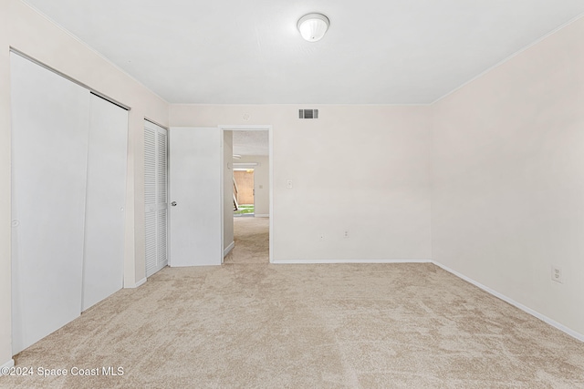 unfurnished bedroom featuring multiple closets, light carpet, and ornamental molding