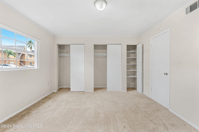 unfurnished bedroom with light carpet, ornamental molding, and multiple closets