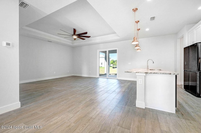 kitchen featuring decorative light fixtures, white cabinets, a raised ceiling, black fridge, and a center island with sink