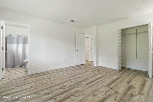 unfurnished bedroom with light wood-type flooring, a textured ceiling, and ensuite bath