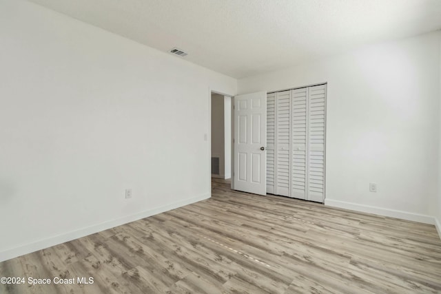 unfurnished bedroom featuring light wood-type flooring, a textured ceiling, and a closet