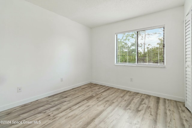 empty room with a textured ceiling and light hardwood / wood-style flooring