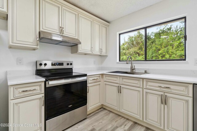 kitchen featuring a textured ceiling, stainless steel electric range oven, sink, and cream cabinets