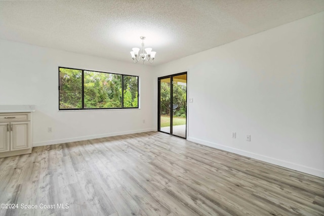 unfurnished room with a textured ceiling, an inviting chandelier, and light hardwood / wood-style flooring