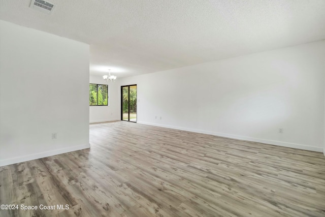 unfurnished room featuring light hardwood / wood-style floors, a textured ceiling, and a chandelier