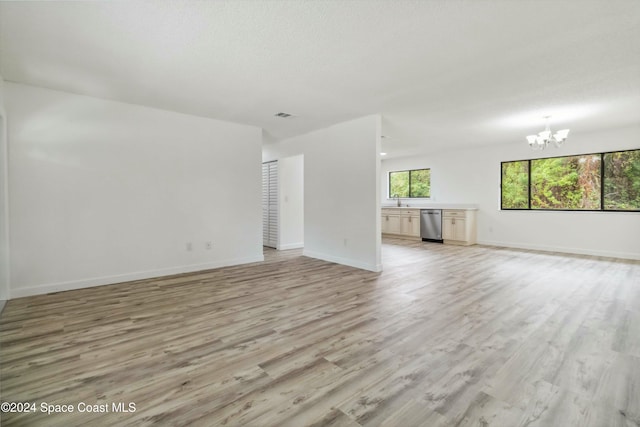 unfurnished living room featuring a textured ceiling, a notable chandelier, light hardwood / wood-style floors, and sink