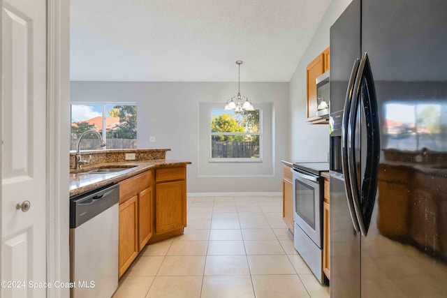 kitchen featuring an inviting chandelier, sink, appliances with stainless steel finishes, decorative light fixtures, and light stone counters