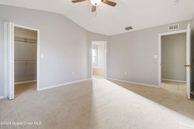 unfurnished bedroom with lofted ceiling, light carpet, ensuite bath, ceiling fan, and a closet