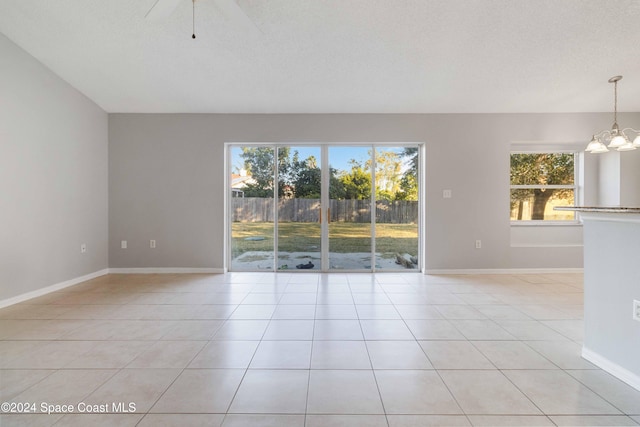 unfurnished room with ceiling fan with notable chandelier, light tile patterned floors, and a textured ceiling