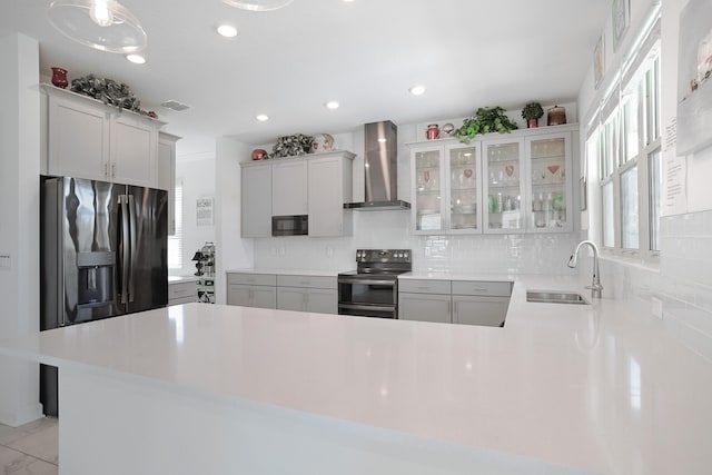 kitchen featuring kitchen peninsula, wall chimney exhaust hood, stainless steel appliances, sink, and hanging light fixtures