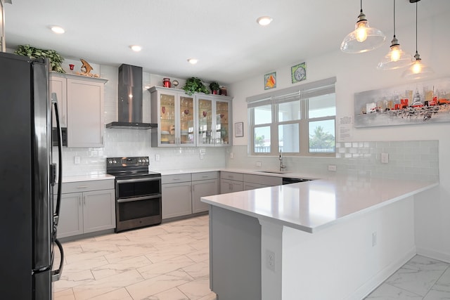 kitchen with wall chimney range hood, appliances with stainless steel finishes, tasteful backsplash, decorative light fixtures, and kitchen peninsula