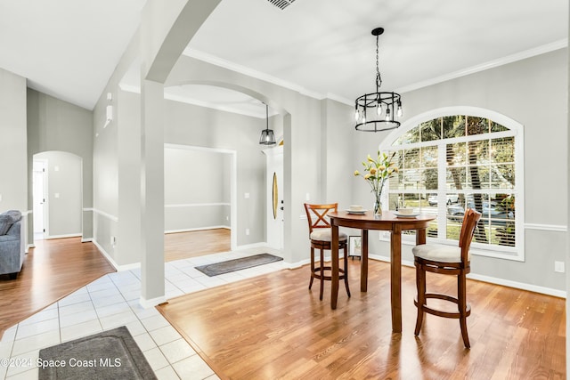 dining space with an inviting chandelier, ornamental molding, vaulted ceiling, and light wood-type flooring